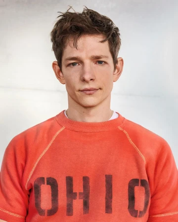 Portrait of an adult male with short brown hair, wearing an orange t-shirt with 'OHIO' printed in black letters, in a studio setting.