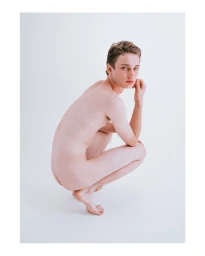 Portrait of a young man crouching against a plain white studio background by Jack Pierson