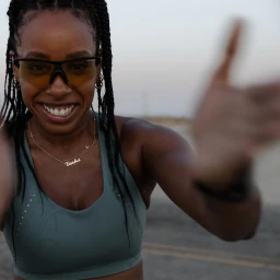 Smiling Black woman wearing yellow-tinted sports glasses and a sage green sports bra outdoors