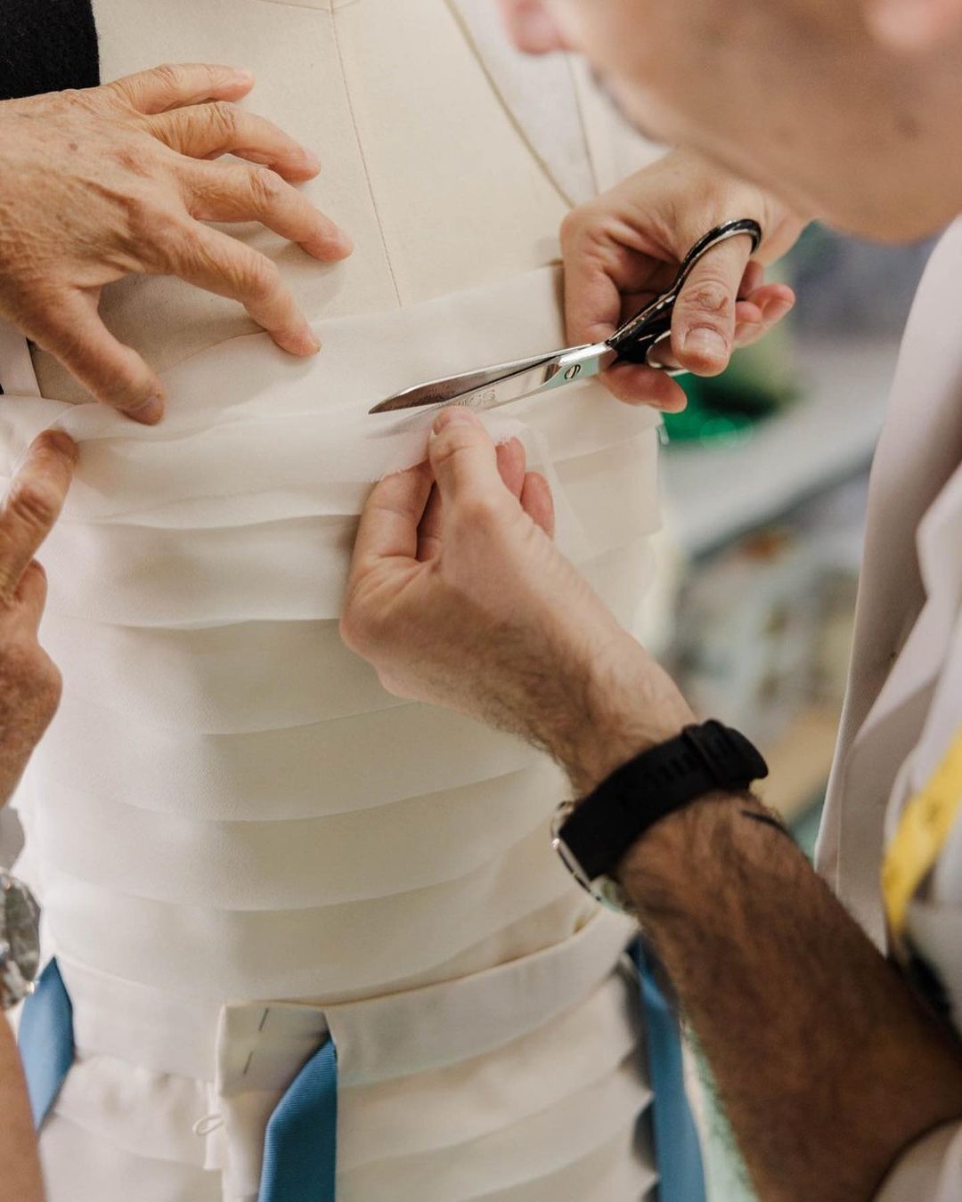 Close-up of a fashion designer fitting a white fabric garment on a mannequin, using scissors. The scene is well-lit and focused.