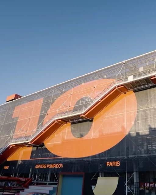 Exterior of the Centre Pompidou in Paris, featuring orange accents, architectural details, and a clear blue sky.