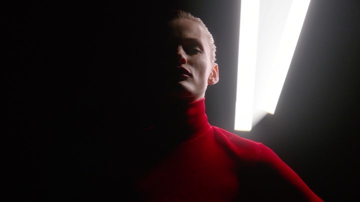 Woman in red turtleneck with strategic lighting creates dramatic shadows in studio. Fashion, beauty, and portrait photography.