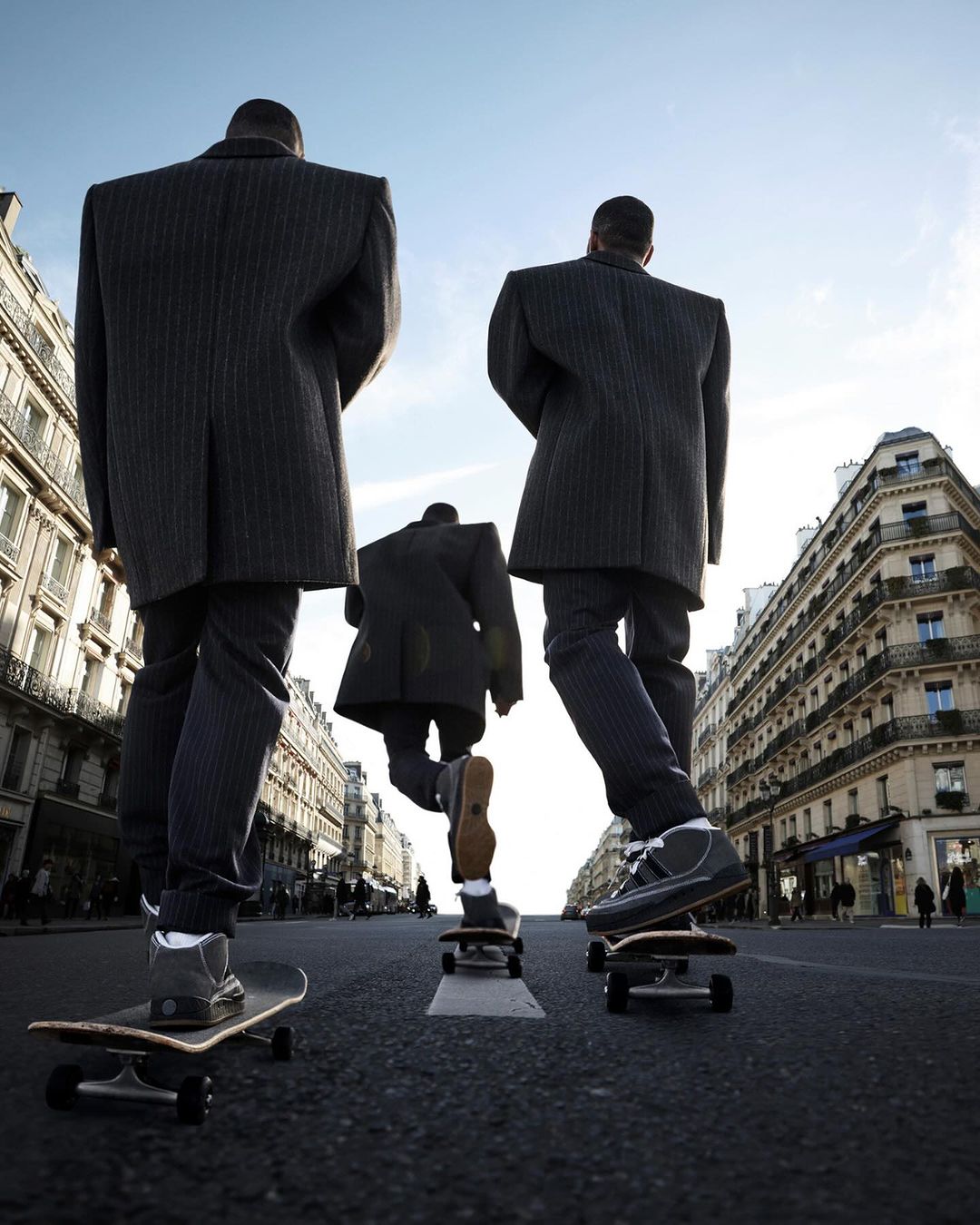 Three business people in suits skateboard on a city street with buildings in the background, shot from a low angle perspective.
