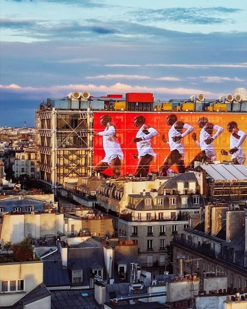 Multiple exposures show a Black male figure running across the top of an orange building with the Paris cityscape visible in the background.