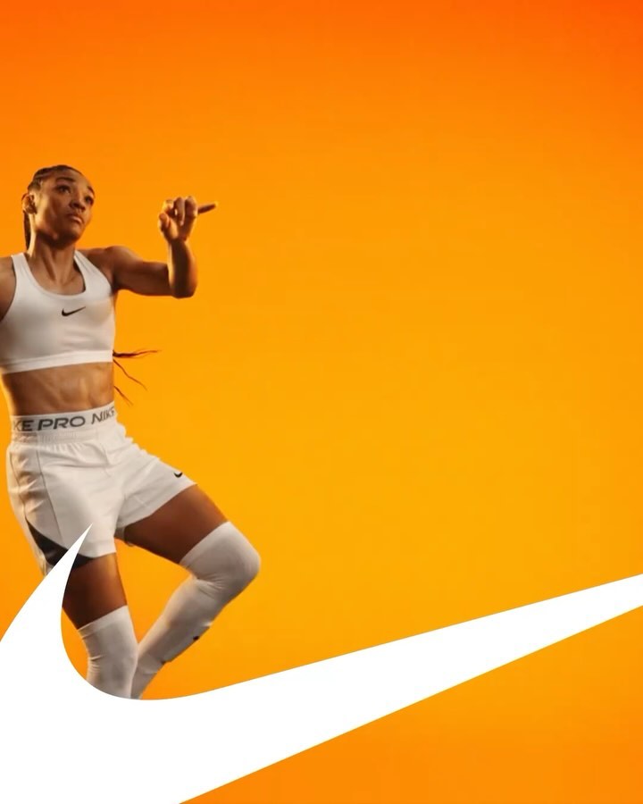 Athletic woman in sports bra and shorts poses dynamically on an orange background with the white Nike swoosh logo.
