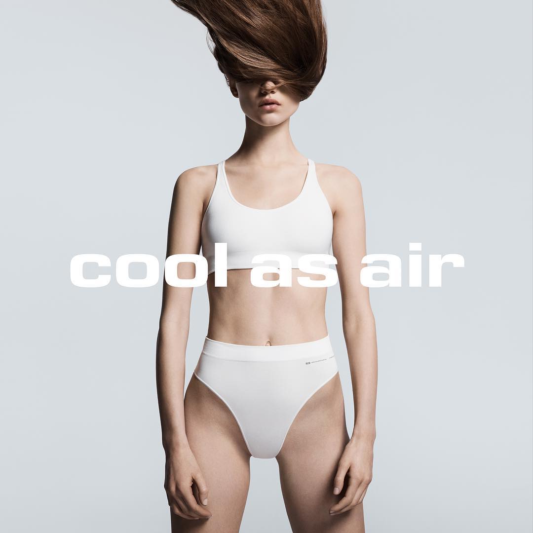 Woman in white underwear and sports bra posing against a light gray backdrop with her brown hair flying above her head.
