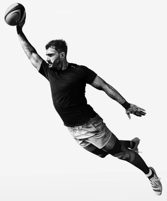 Monochrome shot of a man in mid-air, catching a football with one hand. The background is a solid white, high contrast, action pose.