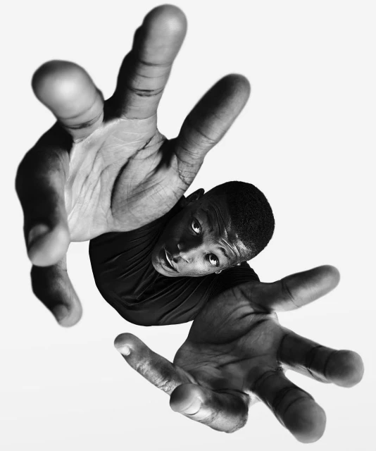 Black and white portrait of a young man with hands raised towards the camera, creating a dramatic and dynamic composition on white.