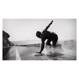 Monochrome action shot of a person sliding on a wet road next to the ocean, captured by Jacob Sutton.