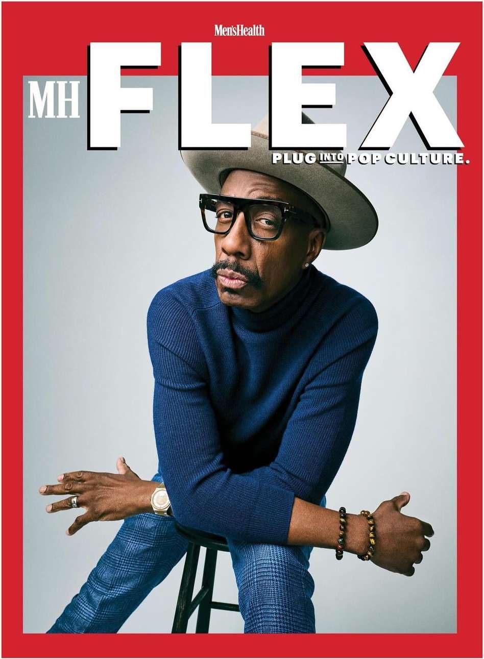 Magazine cover featuring a stylish Black man wearing a hat and glasses, sitting on a stool against a light grey backdrop.