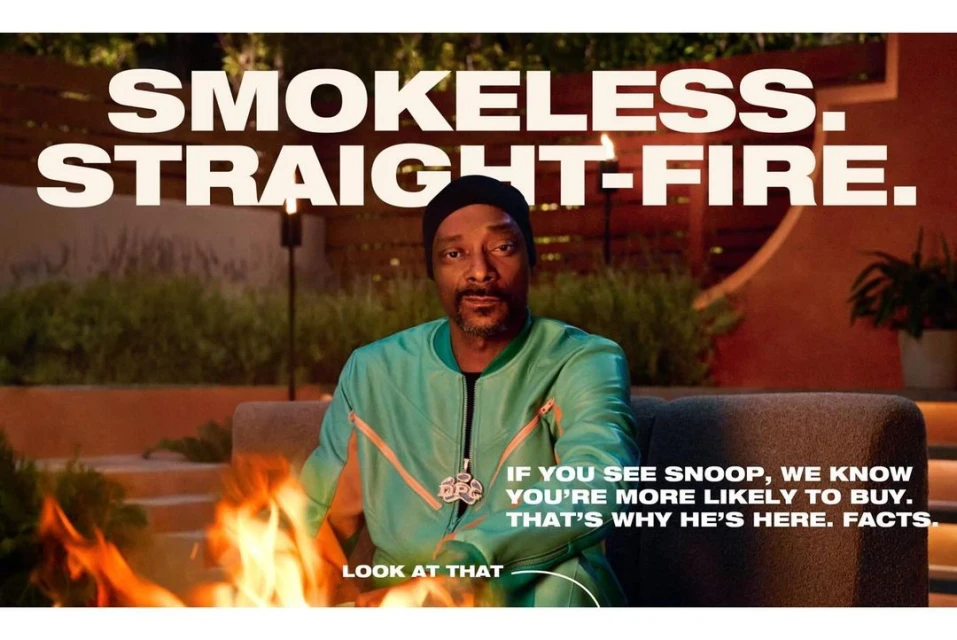 Snoop Dogg poses in a green jacket by a fire pit, promoting smokeless straight-fire. Close-up studio shot with text overlay.