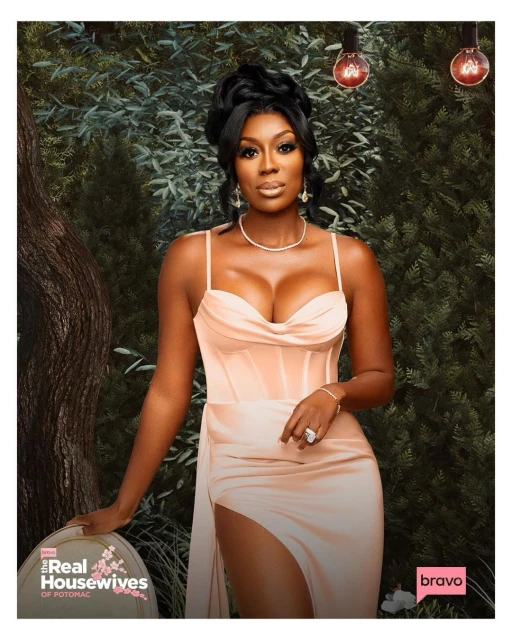 Glamorous woman in a peach-colored dress poses in front of a lush green backdrop with vintage bulbs, showcasing elegance and style.