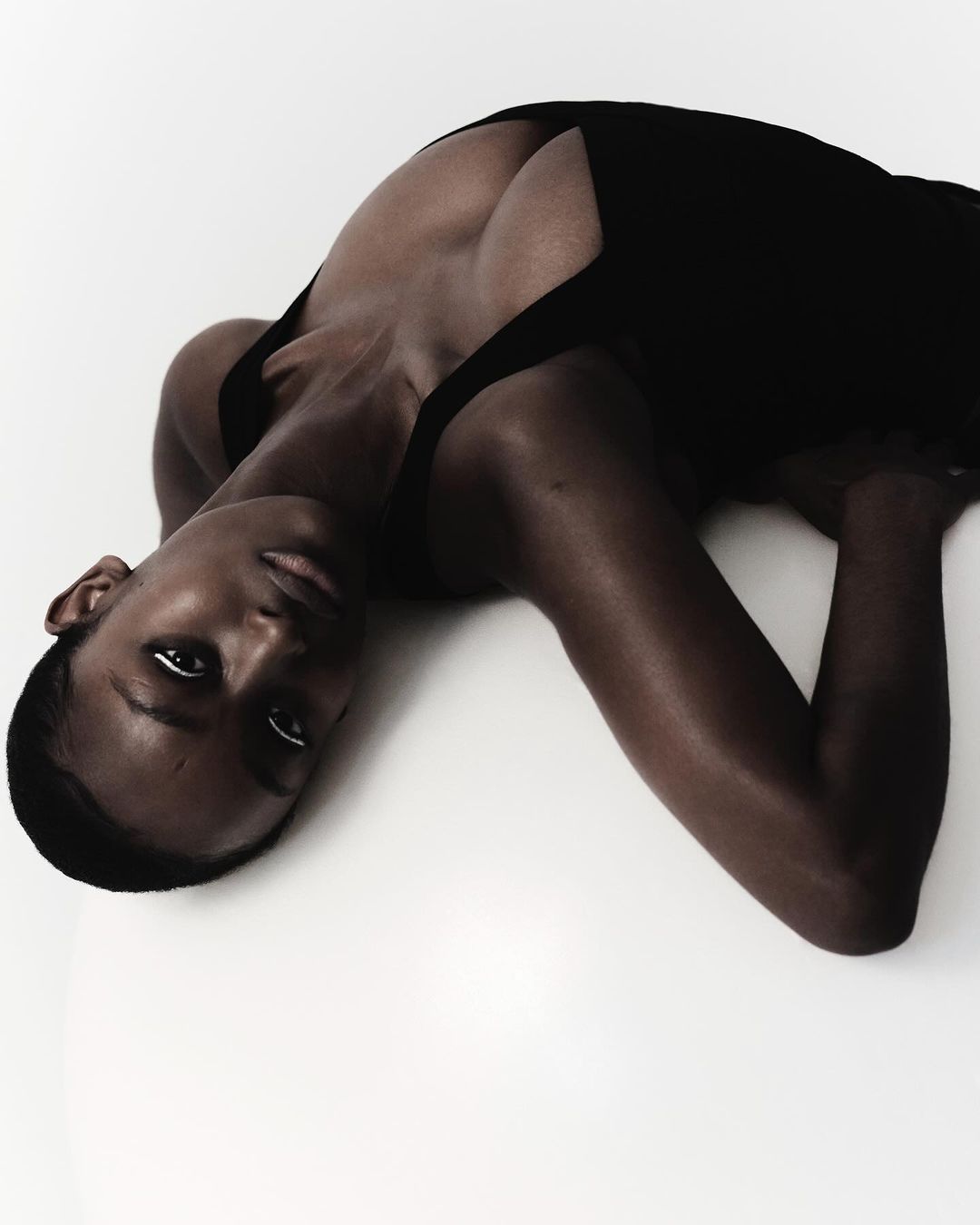 Close-up of an African American woman lying on her side in a dark top against a white background, studio lighting, fashion style.