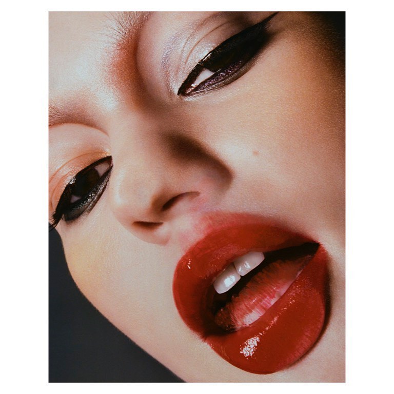 Extreme close-up of a woman's face with bold makeup; bright red lipstick, dramatic eyeliner, and visible teeth.