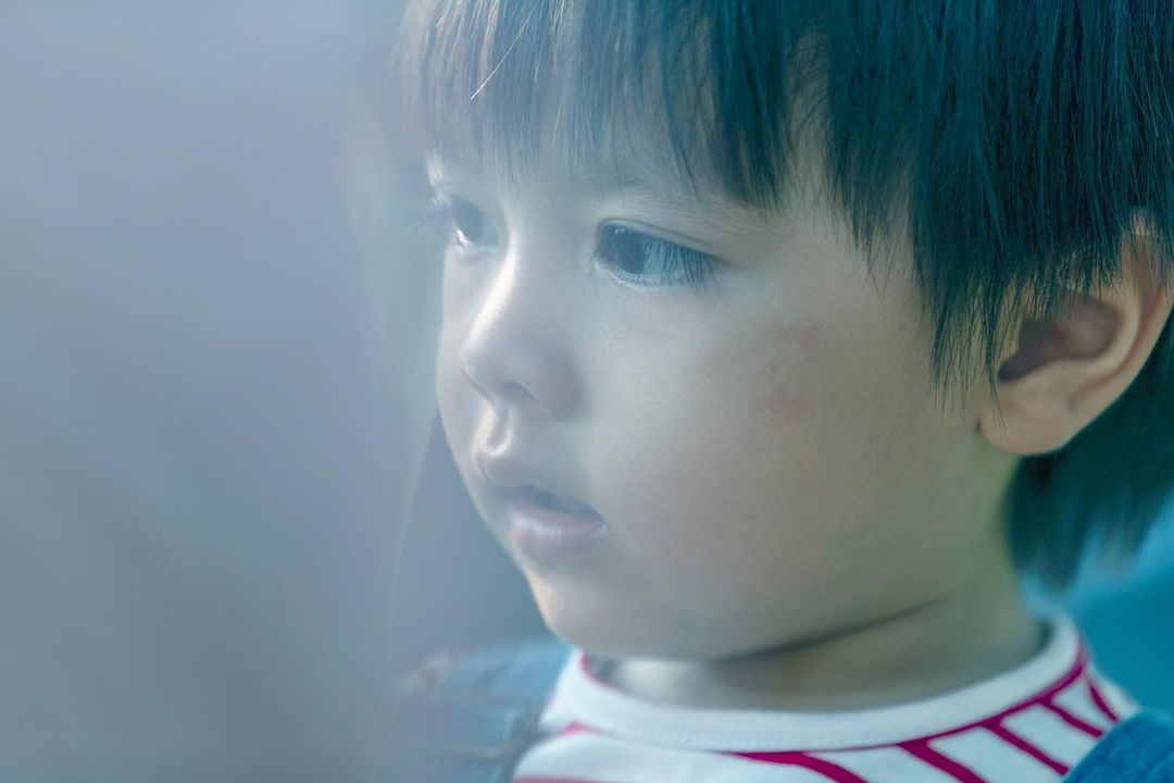 Close-up portrait of a young child with dark hair, gazing thoughtfully with soft lighting, featuring a shallow depth of field.