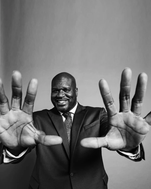 Black and white portrait of a smiling adult male in a suit, holding his open hands toward the camera against a gray background.