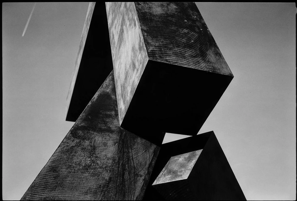 Abstract sculpture of geometric shapes in black and white against a sky backdrop, creating a modern art composition.