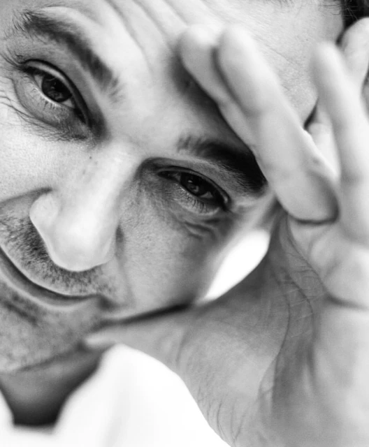 Black and white portrait of an adult male with his hand on his forehead, looking directly at the camera with a thoughtful expression.