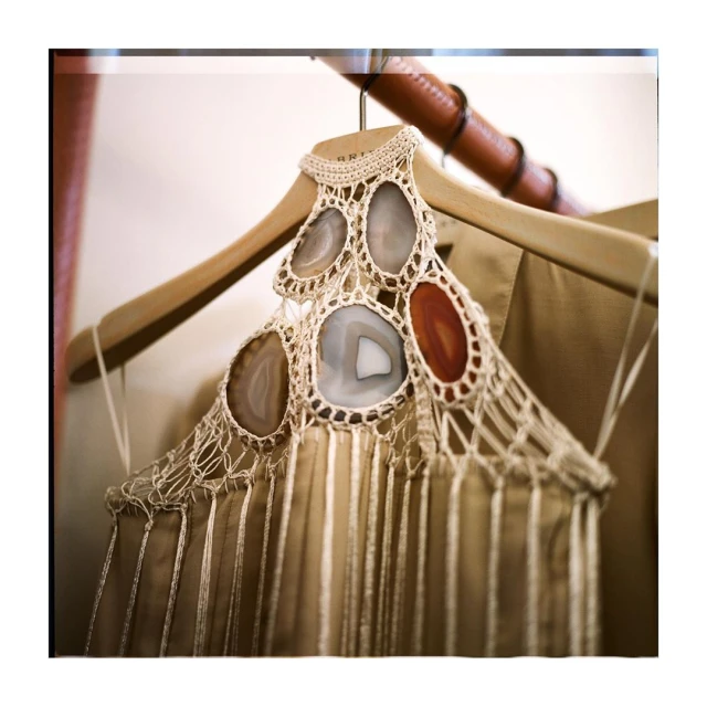 Close-up of a handcrafted macrame top adorned with agate slices hanging from a wooden hanger against a neutral-toned garment backdrop.