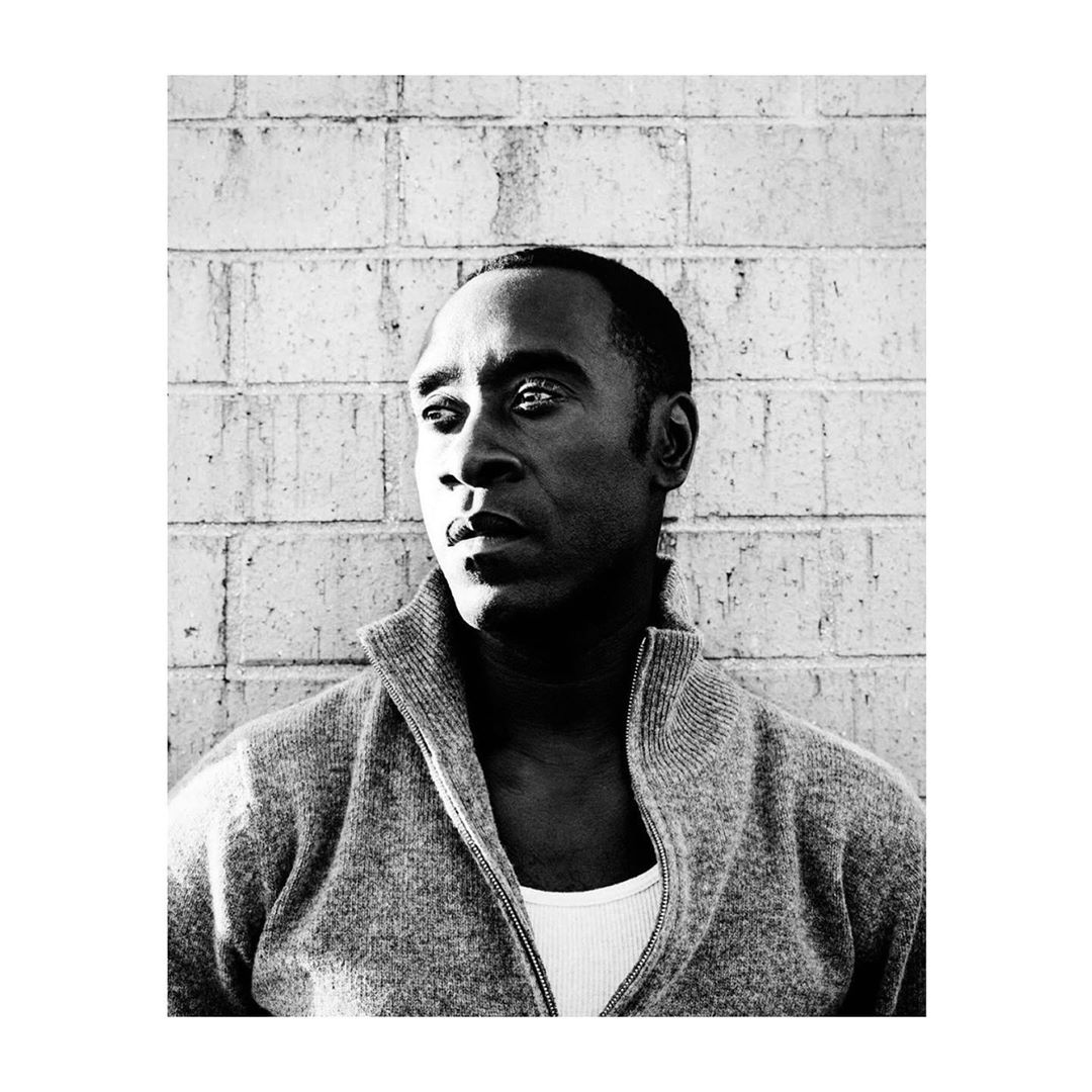 Black and white portrait of a man in a cardigan, facing left, with a textured brick wall background, creating a stark, high-contrast image.