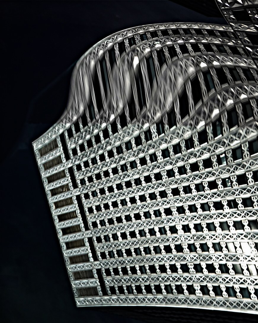 Low angle view of the steel and glass facade of a modern building with patterned cladding against a dark sky, captured at night.