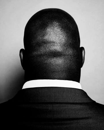 Black and white portrait of an adult male, bald, wearing a dark business suit and white shirt, close up, with a neutral expression.