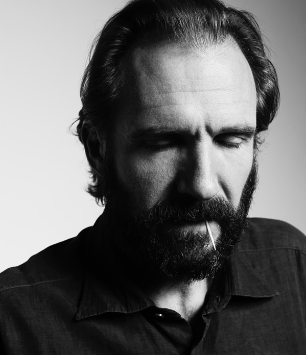 Monochrome portrait of an adult male with a beard and dark hair, wearing a collared shirt, with a toothpick in his mouth, eyes closed.