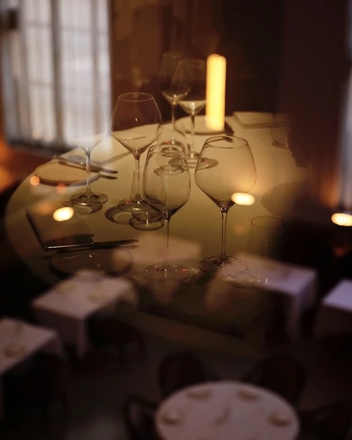An indoor restaurant scene with a long exposure effect showcases set tables with empty wine glasses and soft lighting from pillar candles.