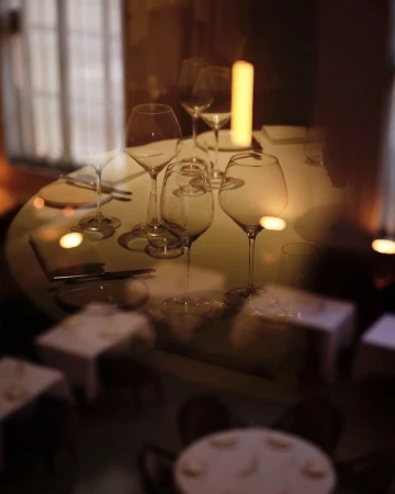 An indoor restaurant scene with a long exposure effect showcases set tables with empty wine glasses and soft lighting from pillar candles.