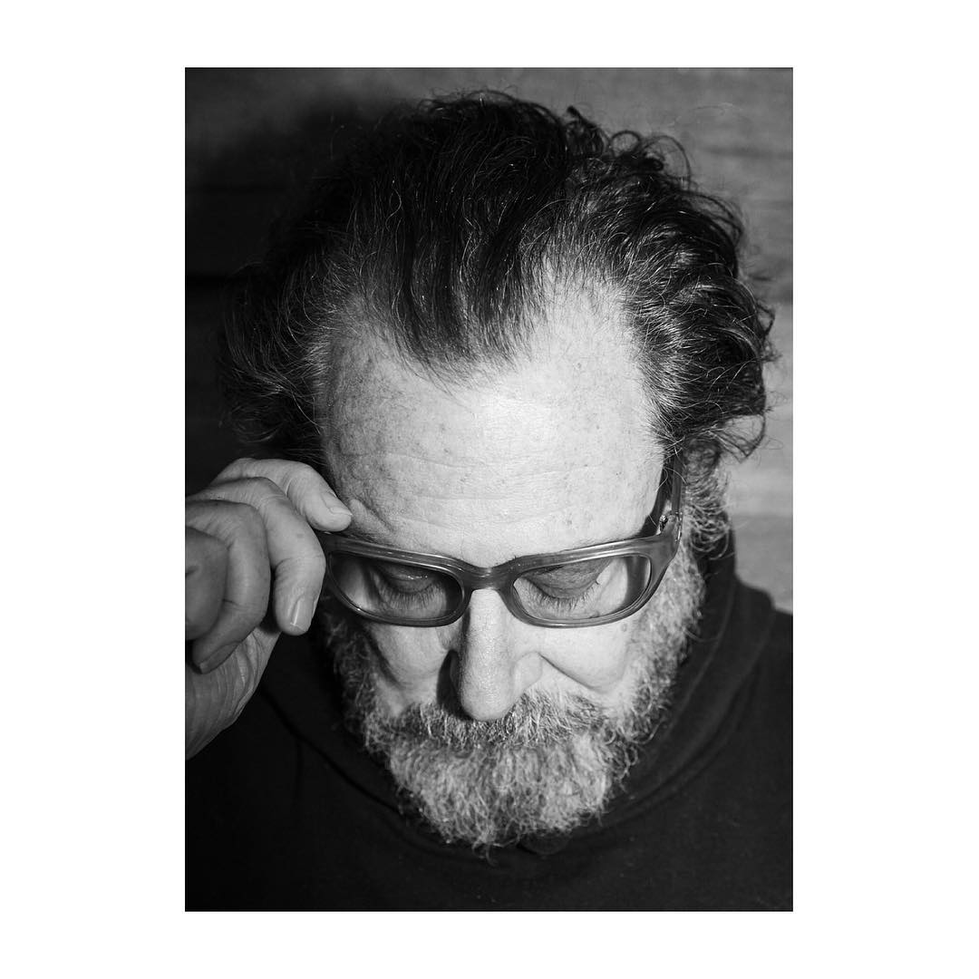 Black and white portrait of an adult man with glasses looking downward, showcasing his facial features and curly hair.