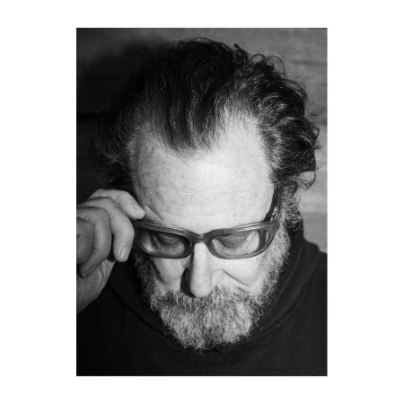 Close-up portrait of a mature man with a beard wearing thick-rimmed glasses and adjusting them, photographed by Jake Chessum.