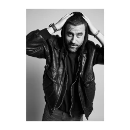 Portrait of a man in a black leather jacket and hoodie holding his head with both hands by photographer Jake Chessum.