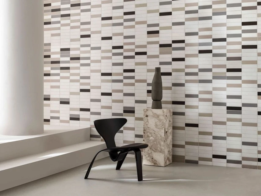 Interior design features modern black chair, sculptural vase, and a wall with horizontally aligned rectangular tiles of various shades.