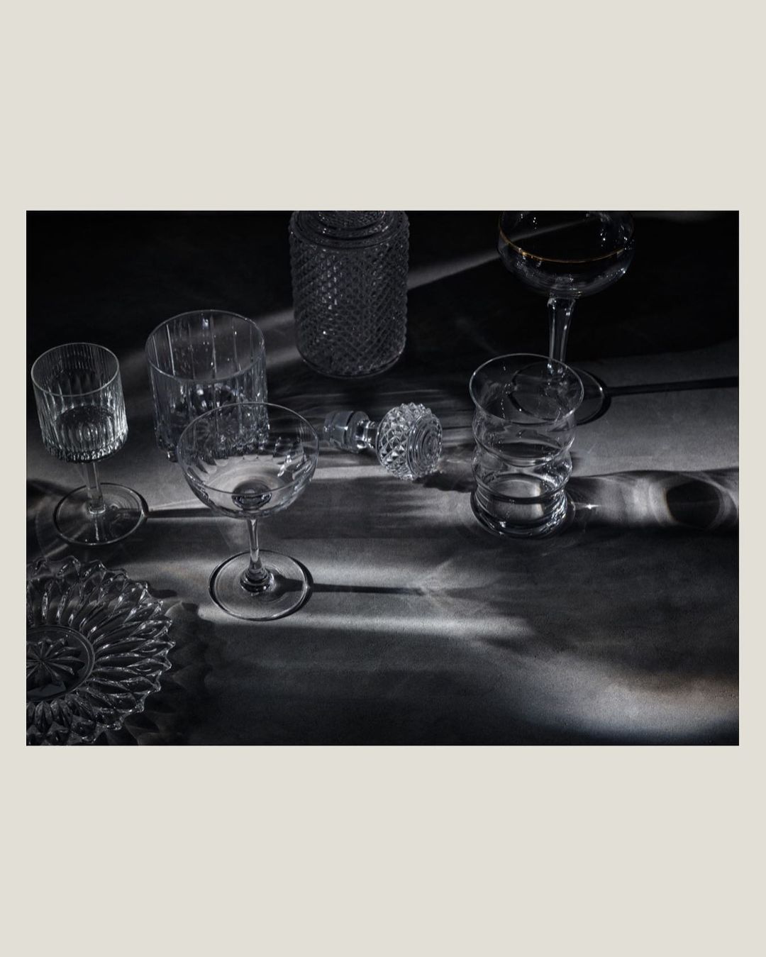 Elegant glassware collection arranged on a dark surface with refracted light creating dynamic shadows and highlights.