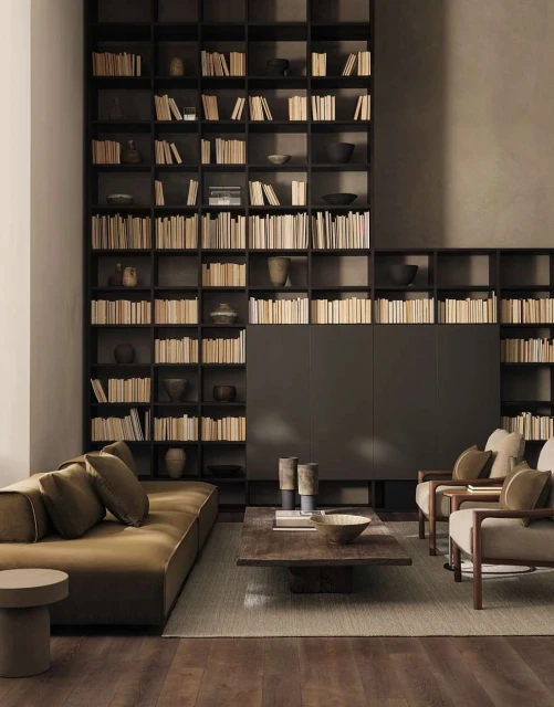 Living room interior with a brown sofa, chairs, a coffee table, and a tall bookshelf filled with books, creating a cozy and inviting space.