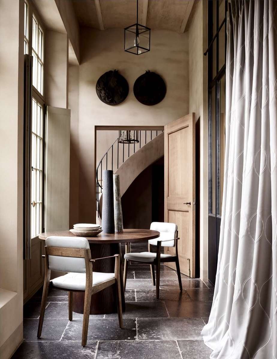 Interior design showcases a dining area with a round wooden table, chairs, and floor-to-ceiling patterned curtains in a neutral color palette.