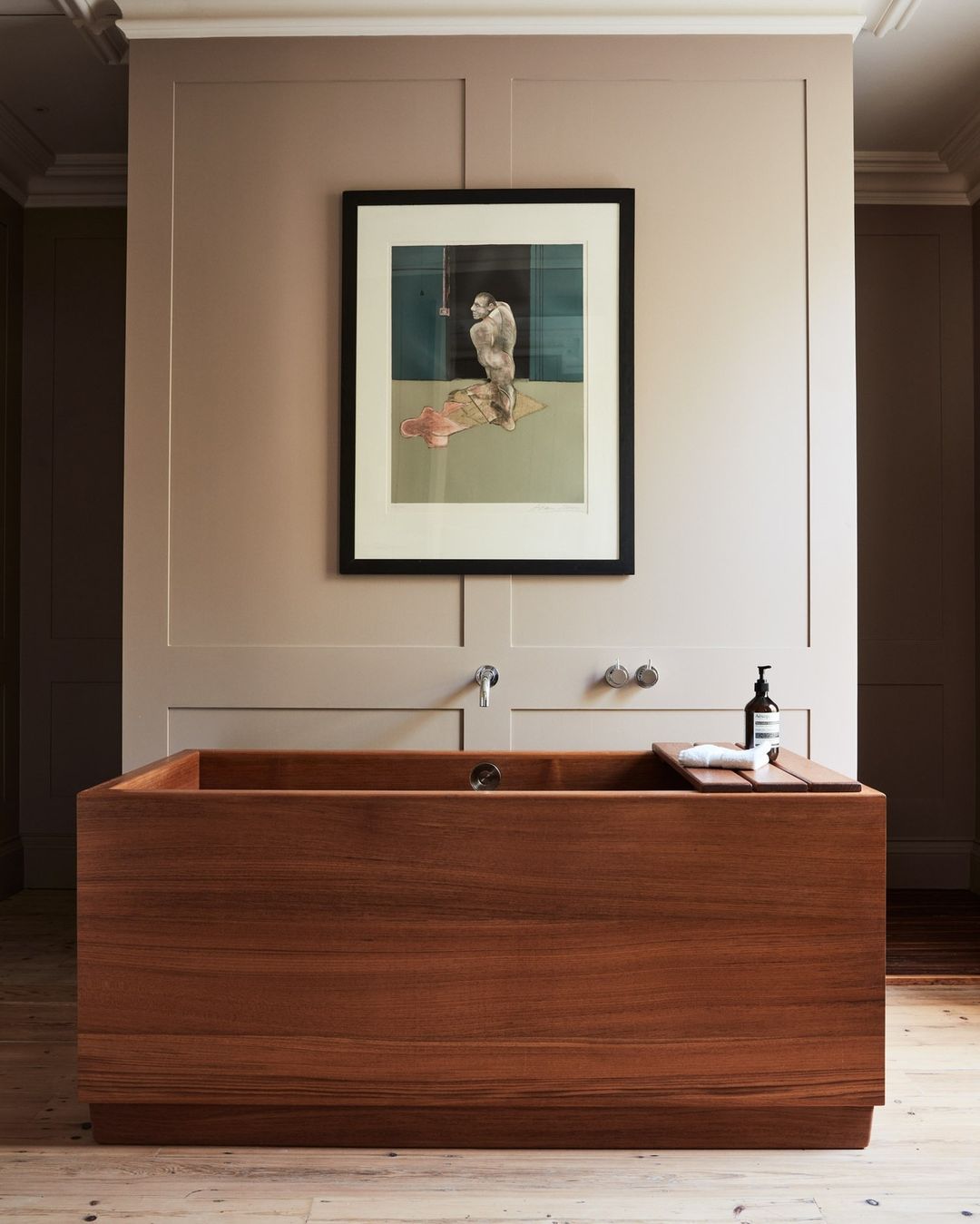 An interior view showcases a wooden bathtub with a framed artwork above, set against a neutral palette in a serene and modern bathroom.