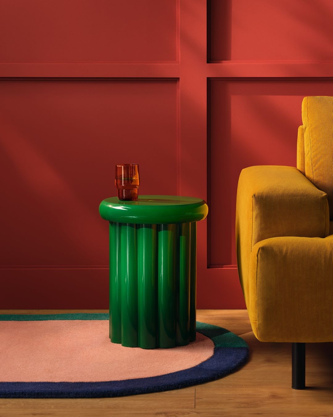 Interior shot featuring a green fluted side table with an amber glass, a yellow corduroy chair, and a red paneled wall for a modern aesthetic.