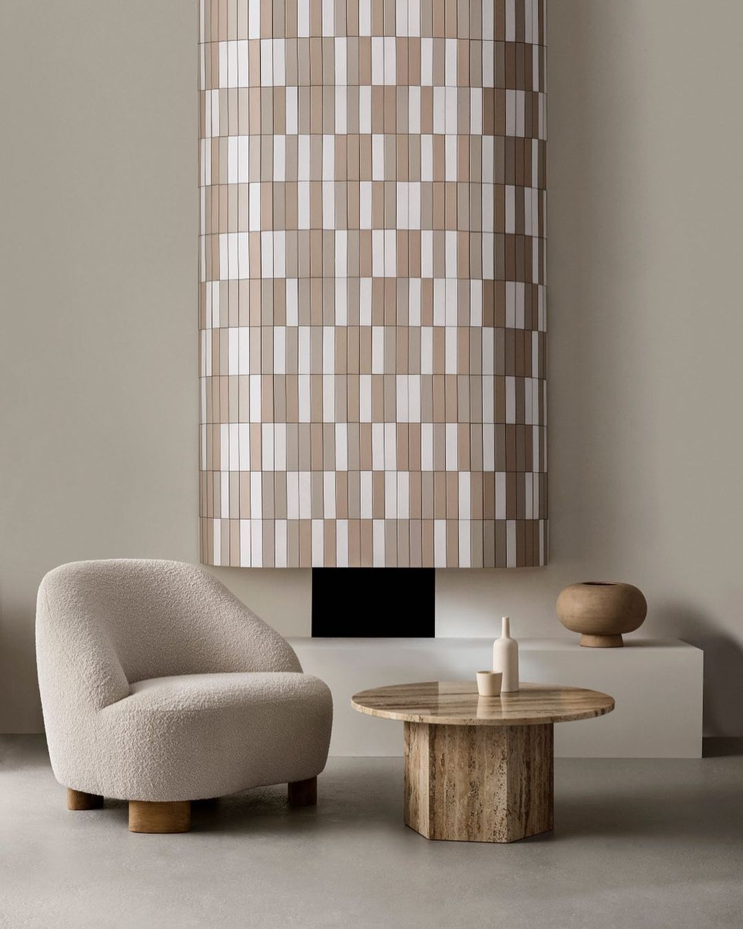 Interior design featuring a beige armchair, marble table with decor, and a textured column against a neutral wall, creating a minimal aesthetic.