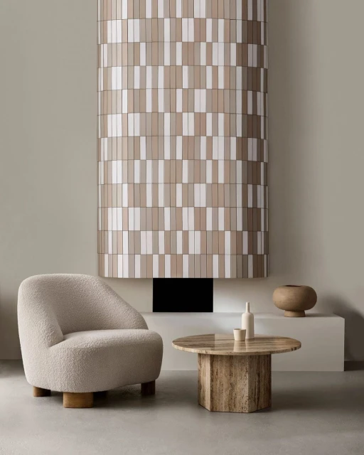 Interior design featuring a beige armchair, marble table with decor, and a textured column against a neutral wall, creating a minimal aesthetic.