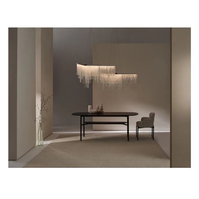 A modern interior with a rectangular dining table, armchair, and glass pendant chandelier against a neutral-toned wall and carpet.