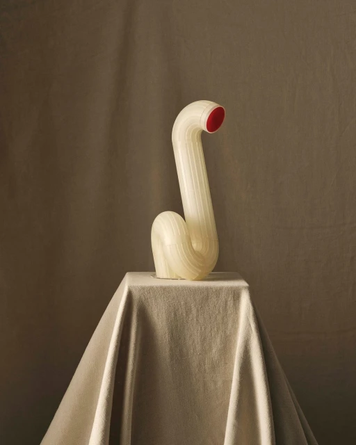 Still life photograph of a contemporary art sculpture on a draped pedestal with an off-white, tan, and red color palette in a photo studio.