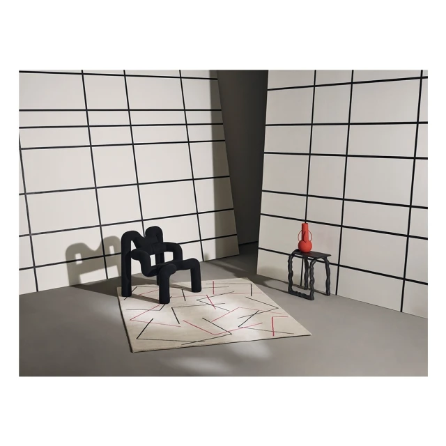 Contemporary interior photo features a black chair, patterned rug, black side table with orange vase against a white-paneled wall.
