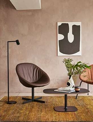 Brown leather chair and dark wood table are positioned on a brown rug in an interior setting with modern art and a sleek lamp.
