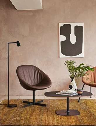 Brown leather chair and dark wood table are positioned on a brown rug in an interior setting with modern art and a sleek lamp.