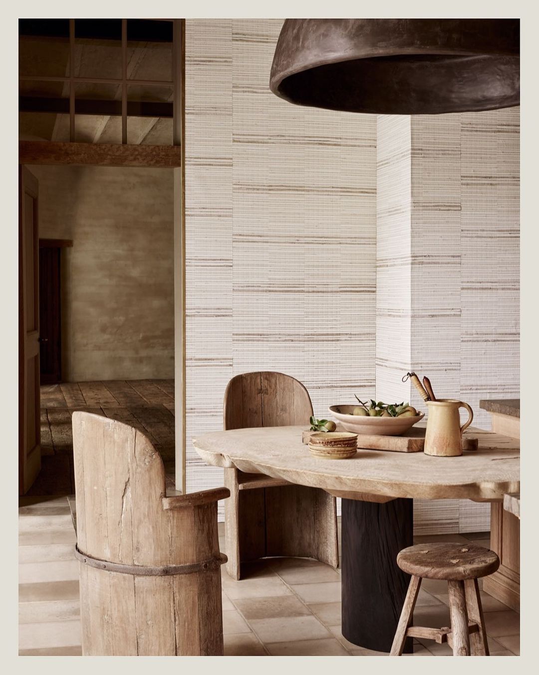 Rustic interior features wooden chairs and table with dishware under a modern light fixture, creating a warm and inviting setting.