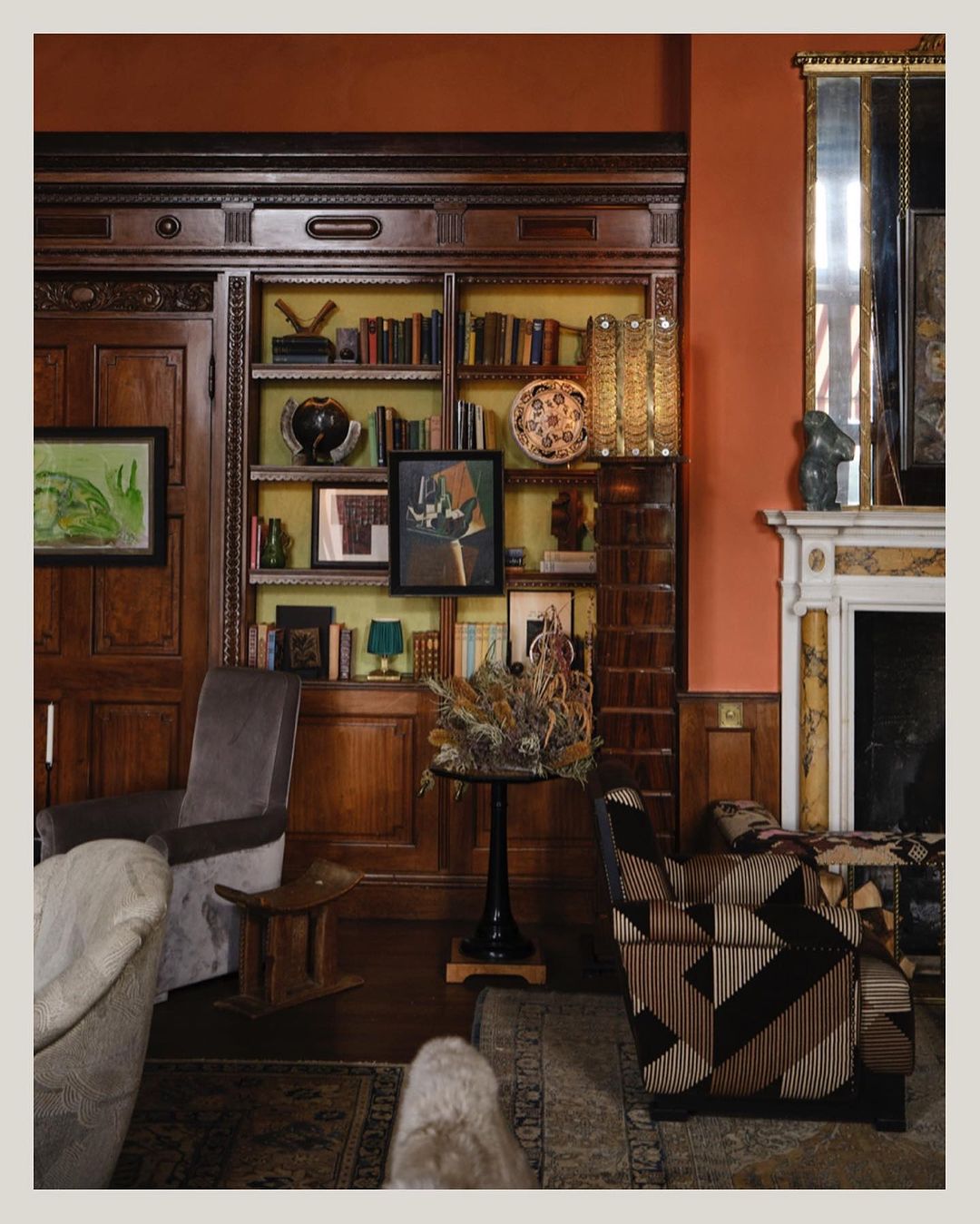 Living room interior with wood paneling, bookshelves, traditional furnishings, artwork, and fireplace, creating a warm, classic atmosphere.