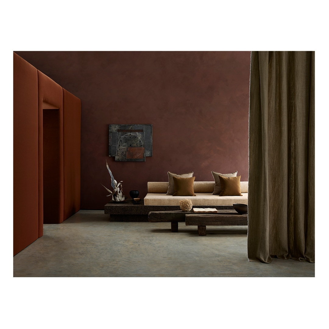 Contemporary interior showcases a neutral sofa with cushions, rustic wood tables, modern art, and a rich earth-toned color palette.