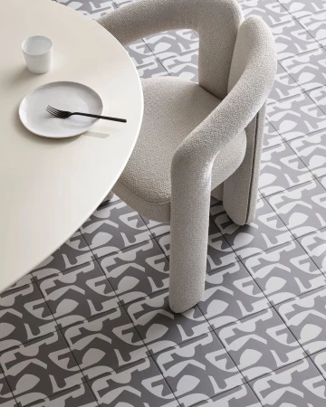 Interior scene featuring a modern chair with curved arms and a round table set with a plate, fork, and cup, set against a patterned tile floor.
