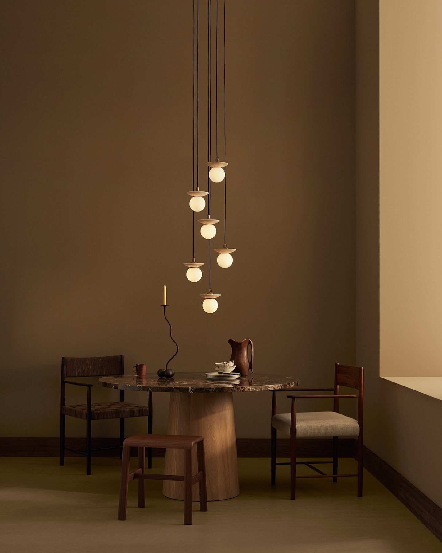 Contemporary interior featuring a dining table set with plates and a pitcher, illuminated by a modern pendant light fixture.